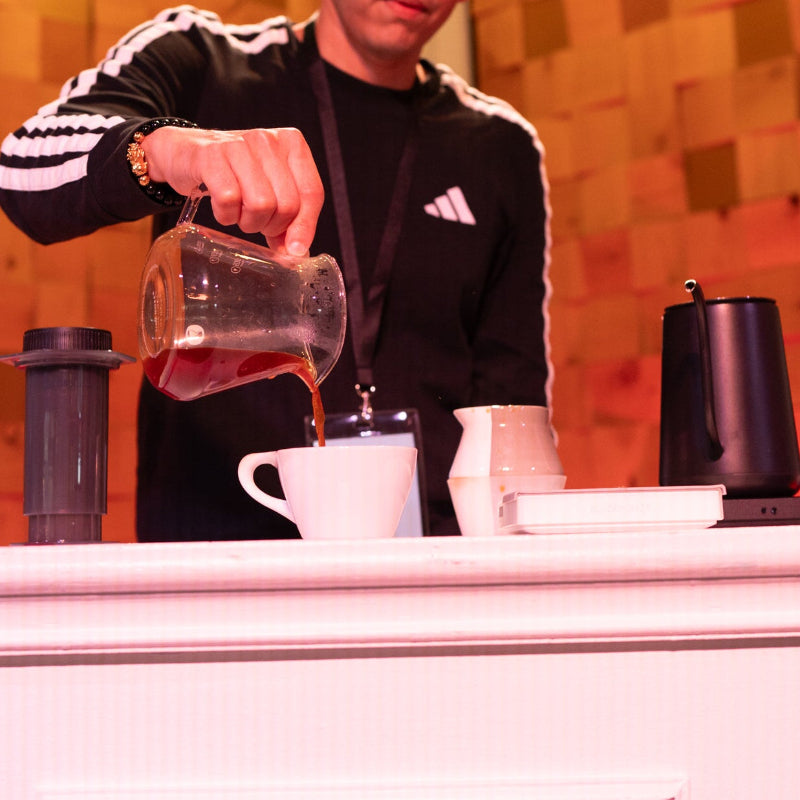 Person pouring a drink behind a bar with a colorful wall in the background